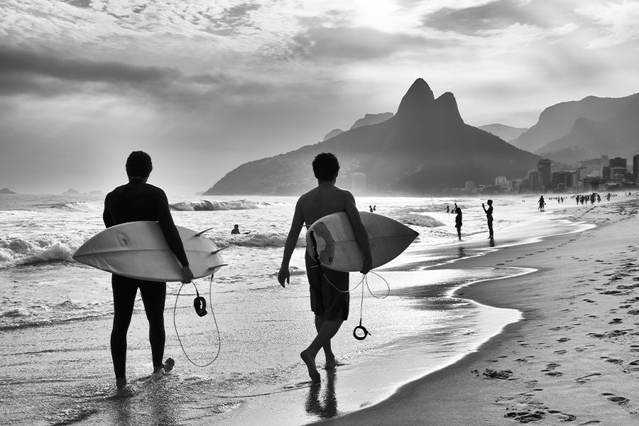 Blog - Surfers Walking on the Beach with City in the Background in Black and White